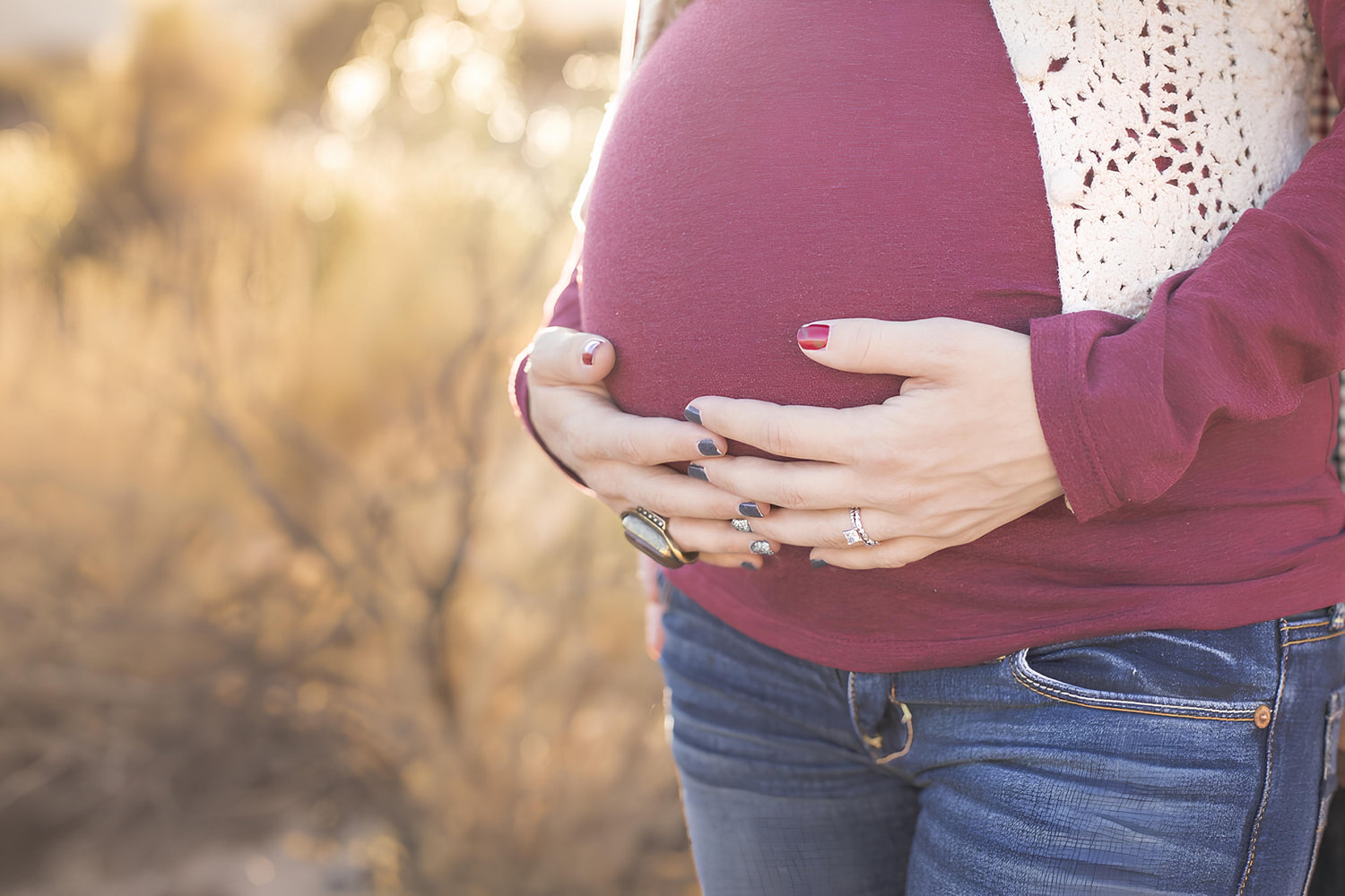 En gravid kvinder der står udenfor og holder på sin mave